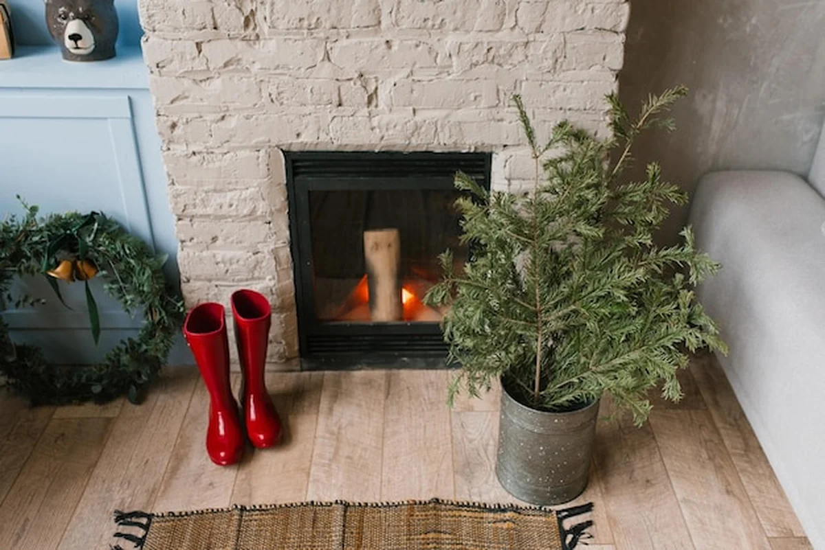 Skandynawski kominek z cegłą, drewnem i dekoracją świąteczną przed szarą ścianą