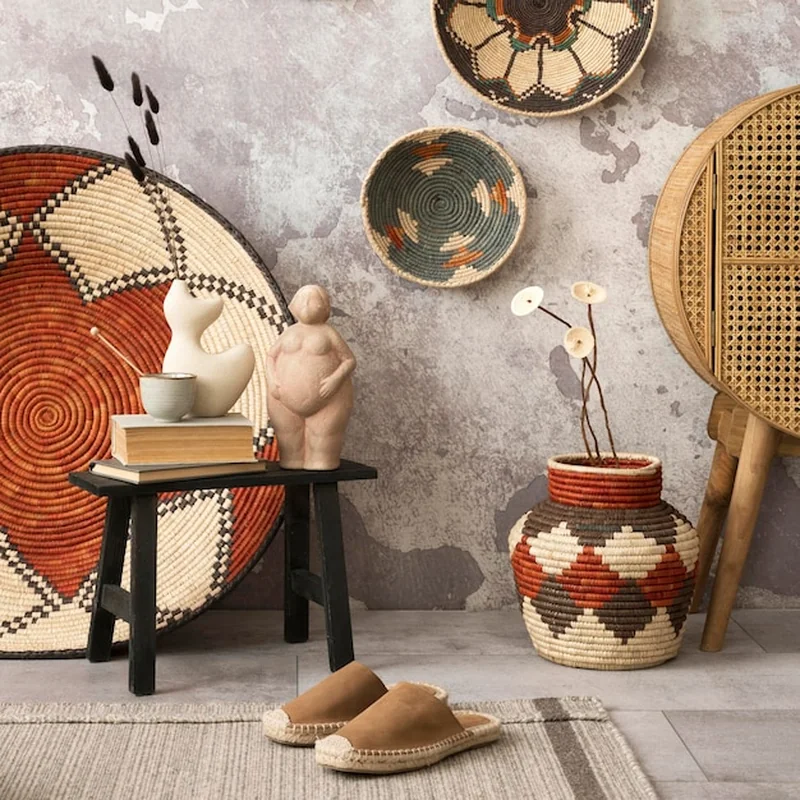 Etniczna kompozycja wnętrza salonu z kolorowymi koszami, rattanowym kredensem i beżowym stołkiem