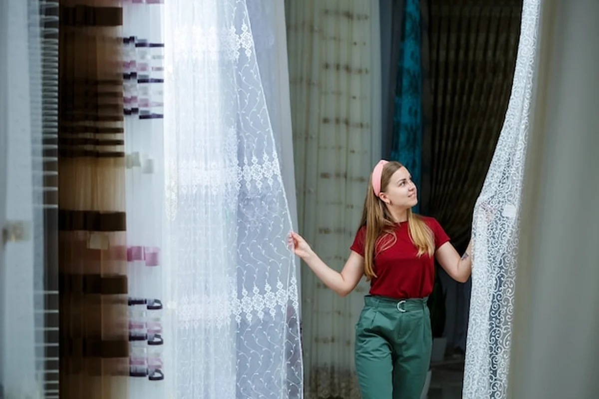 Młoda kobieta wybiera tkaninę na nowe zasłony w sklepie. Próbki zasłony wiszą na wieszakach