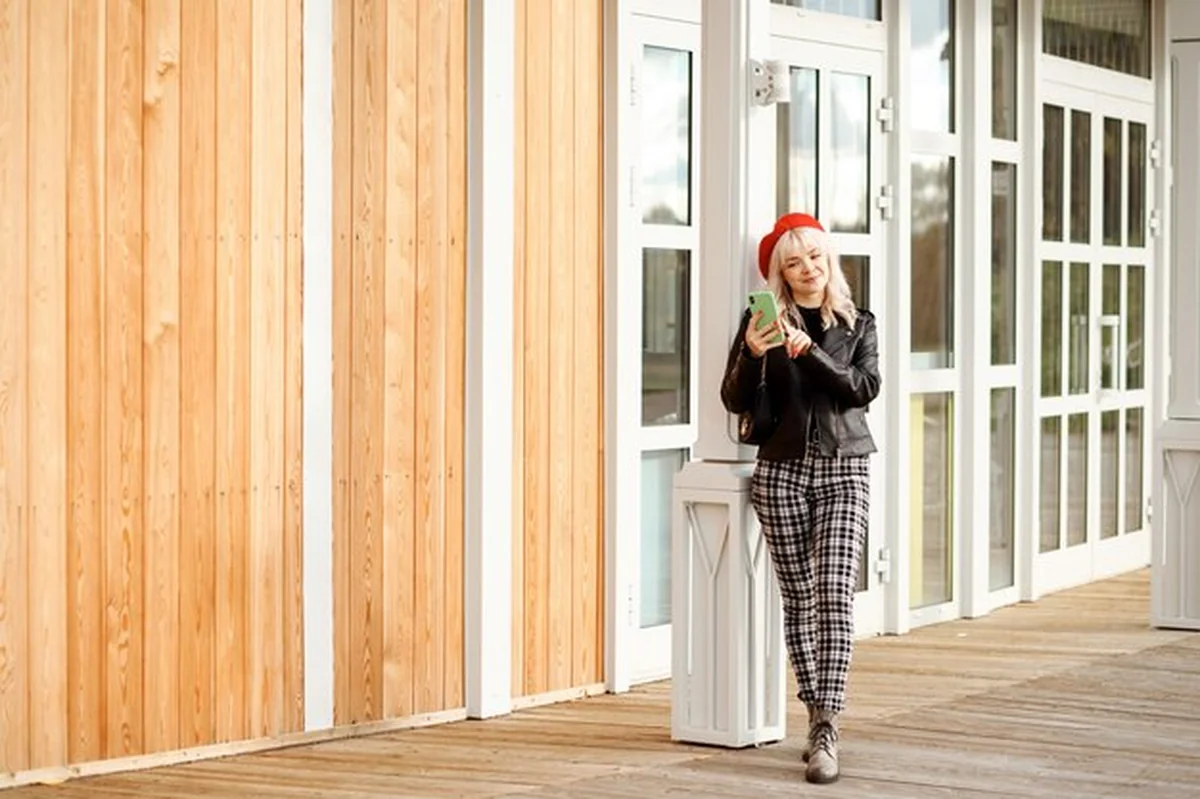 Stylowa kobieta w czarnej skórzanej kurtce, spodnie w kratkę i czerwony beret, rozmawia przez telefon