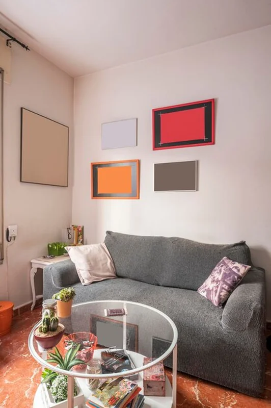 Salon z małą szarą sofą i okrągłym stołem na czerwonych płytkach