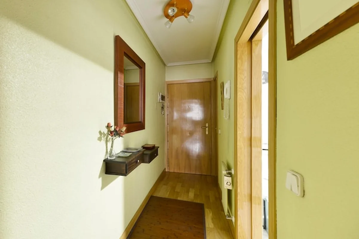 Przedpokój z lustrem w drewnianej ramie, jasnozielonymi ścianami i stolarką dębową